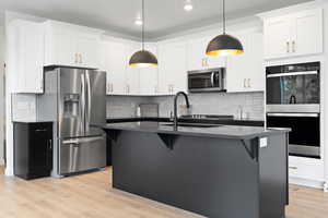 Kitchen with tasteful backsplash, hanging light fixtures, stainless steel appliances, and light hardwood / wood-style floors