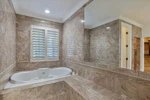 Master Bathroom with a relaxing tiled tub, tile walls, and ornamental molding