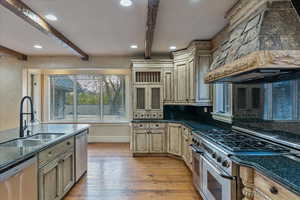 Kitchen featuring premium range hood, sink, light wood-type flooring, appliances with stainless steel finishes, and beam ceiling