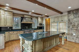 Kitchen featuring black microwave, light hardwood / wood-style flooring, high end stove, a center island with sink, and custom range hood