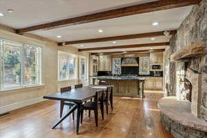 Dining space with beam ceiling, a stone fireplace, light hardwood / wood-style flooring, and sink