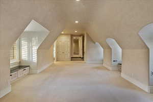 Bonus room with light colored carpet and vaulted ceiling