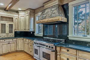 Kitchen with beam ceiling, tasteful backsplash, double oven range, custom range hood, and light wood-type flooring