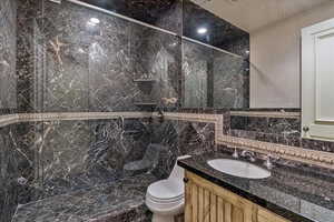 Ensuite bathroom featuring an enclosed shower, vanity, toilet, and tile walls