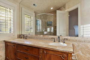 Bathroom with tiled shower, vanity, and plenty of natural light