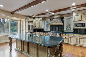 Kitchen with premium range hood, a large island with sink, high end stainless steel range, and tasteful backsplash