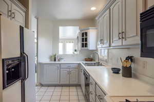 Kitchen featuring light tile patterned flooring, stainless steel dishwasher, white fridge with ice dispenser, and sink