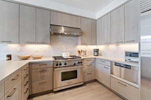 Kitchen featuring decorative backsplash, high end stove, light hardwood / wood-style flooring, and wall chimney range hood