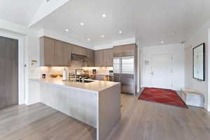 Kitchen with wall chimney exhaust hood, tasteful backsplash, kitchen peninsula, light hardwood / wood-style floors, and stainless steel built in fridge