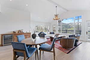 Dining space featuring beam ceiling, wine cooler, light hardwood / wood-style flooring, high vaulted ceiling, and a notable chandelier