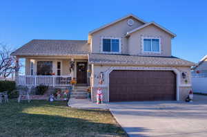 View of front of property with a porch, a garage, and a front lawn