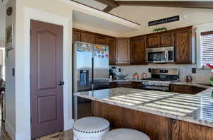 Kitchen with backsplash, vaulted ceiling with beams, light stone countertops, and stainless steel appliances