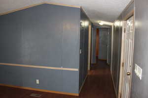 Corridor with a textured ceiling, dark hardwood / wood-style flooring, and lofted ceiling