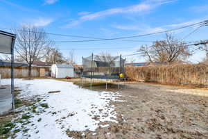 Yard layered in snow with a storage shed and a trampoline