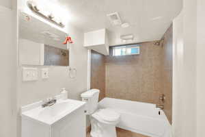 Full bathroom featuring vanity, a textured ceiling, tiled shower / bath combo, and toilet