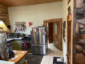 Kitchen featuring appliances with stainless steel finishes, tile patterned floors, wood ceiling, green cabinetry, and wood walls