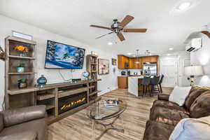 Living room featuring a textured ceiling, light wood-type flooring, a wall unit AC, and ceiling fan