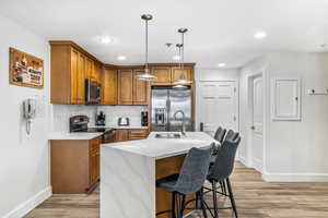 Kitchen with sink, hanging light fixtures, an island with sink, appliances with stainless steel finishes, and light wood-type flooring