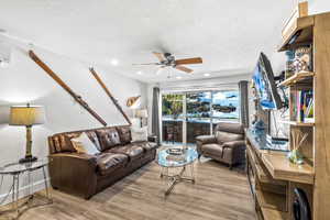 Living room with a textured ceiling, light wood-type flooring, and ceiling fan