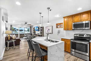 Kitchen with a center island with sink, sink, ceiling fan, light wood-type flooring, and stainless steel appliances