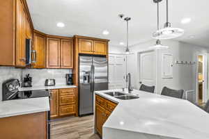 Kitchen with sink, stainless steel appliances, light stone counters, an island with sink, and light wood-type flooring