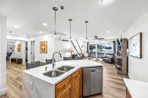 Kitchen with dishwasher, a kitchen island with sink, sink, hanging light fixtures, and light hardwood / wood-style floors