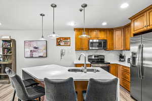 Kitchen featuring appliances with stainless steel finishes, sink, a center island with sink, light hardwood / wood-style flooring, and hanging light fixtures