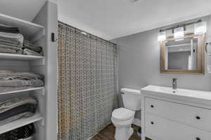 Bathroom with curtained shower, hardwood / wood-style floors, a textured ceiling, toilet, and vanity