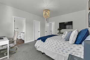 Bedroom featuring connected bathroom, a chandelier, and dark colored carpet