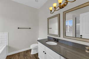 Bathroom with hardwood / wood-style flooring, vanity, toilet, and tiled bath