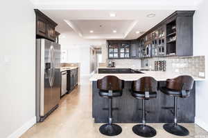 Kitchen featuring backsplash, a kitchen breakfast bar, appliances with stainless steel finishes, a tray ceiling, and kitchen peninsula