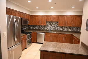 Kitchen featuring decorative backsplash, stainless steel appliances, sink, dark stone countertops, and light tile patterned flooring