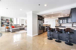 Kitchen with decorative backsplash, stainless steel refrigerator with ice dispenser, a kitchen bar, ornamental molding, and a kitchen island