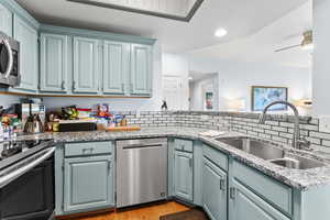 Kitchen with decorative backsplash, stainless steel appliances, ceiling fan, sink, and light hardwood / wood-style floors