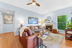 Living room with a tile fireplace, ceiling fan, and light wood-type flooring