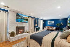 Bedroom with a fireplace, wood-type flooring, and a textured ceiling