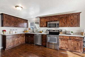 Kitchen featuring a textured ceiling, dark hardwood / wood-style flooring, stainless steel appliances, and sink