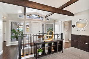 Interior space with a textured ceiling, lofted ceiling with beams, and dark hardwood / wood-style floors