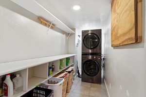 Laundry area featuring a textured ceiling, light tile patterned floors, and stacked washer / drying machine