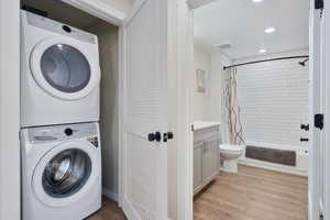 Laundry room with stacked washer and dryer and light hardwood / wood-style floors