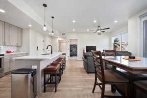 Kitchen with gray cabinetry, ceiling fan, an island with sink, pendant lighting, and light hardwood / wood-style floors