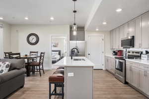 Kitchen featuring gray cabinetry, stainless steel appliances, decorative light fixtures, a center island with sink, and light wood-type flooring