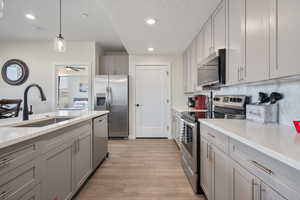 Kitchen with pendant lighting, sink, gray cabinets, appliances with stainless steel finishes, and light hardwood / wood-style floors