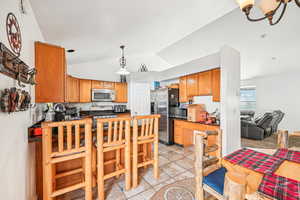 Kitchen with stainless steel appliances, an inviting chandelier, kitchen peninsula, vaulted ceiling, and light tile patterned flooring