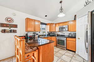 Kitchen featuring hanging light fixtures, kitchen peninsula, vaulted ceiling, a kitchen bar, and appliances with stainless steel finishes