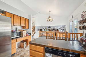 Kitchen featuring french doors, stainless steel appliances, vaulted ceiling, decorative light fixtures, and a notable chandelier