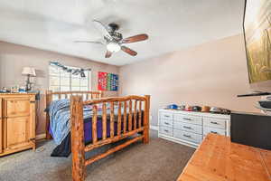 Bedroom with ceiling fan, a textured ceiling, and dark colored carpet