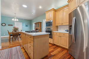 Kitchen with dark hardwood / wood-style floors, a chandelier, decorative light fixtures, a kitchen island, and appliances with stainless steel finishes