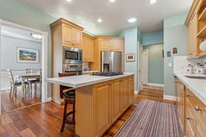 Kitchen with a breakfast bar, stainless steel appliances, dark hardwood / wood-style flooring, light brown cabinetry, and a kitchen island