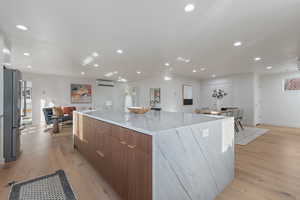 Kitchen with a large island, light stone countertops, an AC wall unit, stainless steel fridge, and light wood-type flooring